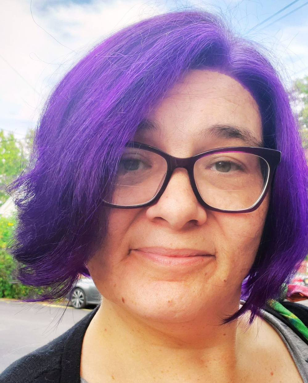 Kat, a woman with purple hair and glasses looks at the camera