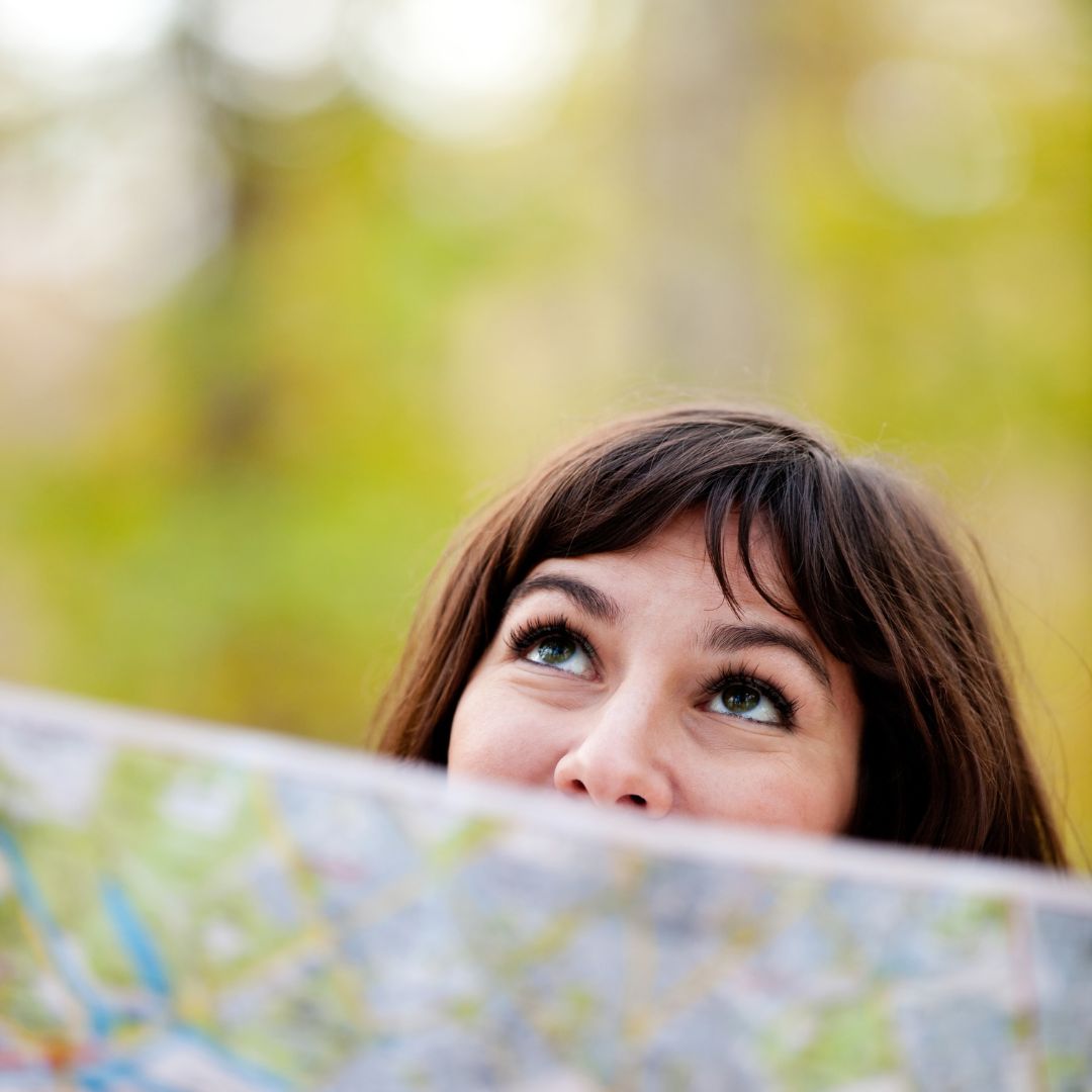 image of a human with dark hair looking upward and peering over a map